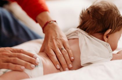 Infante disteso prono massaggiato sulla schiena da due mani di adulto